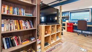 Una habitación con estanterías de madera llenas de libros, un televisor de pantalla plana, un escritorio con computadora y un archivador rojo.