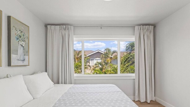 A bedroom with a large bed, a window with curtains, and a painting on the wall.