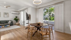 A spacious living room with a wooden floor, a grey sofa, a coffee table, and a TV on a stand.
