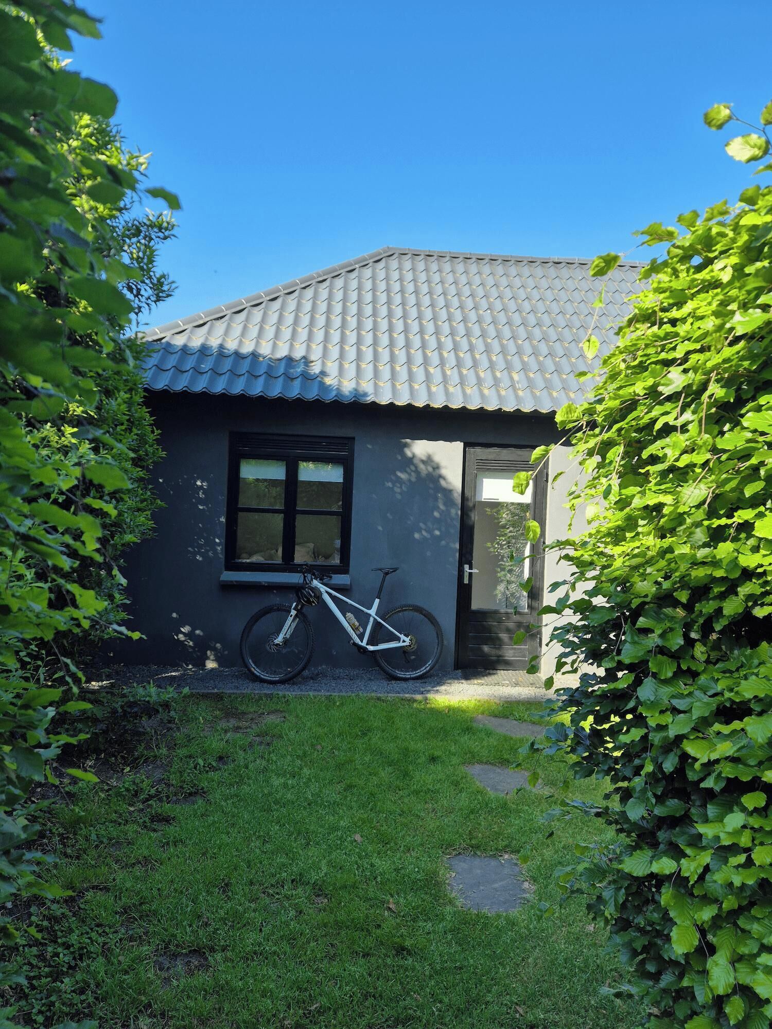 Une petite maison avec un toit en tuiles, un vélo garé devant et une cour couverte d’herbe.
