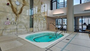 An indoor swimming pool with a marble wall, emergency stop button, public spa jet pump timer switch, and a view of the outside through large windows. - Watch planes takeoff from your balcony! 2+1 BD 2 BA w/ pool, hot tub & parking (Toronto)