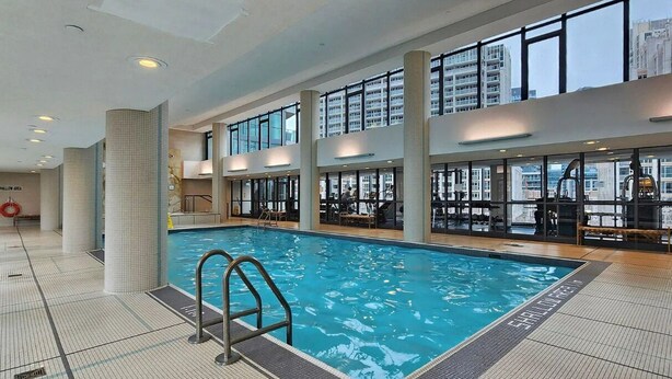 An indoor swimming pool with clear glass walls, a tiled floor, and a visible "SHALLIWATER" label. - Watch planes takeoff from your balcony! 2+1 BD 2 BA w/ pool, hot tub & parking (Toronto)
