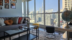 A modern living room with a large window, a sofa, a coffee table, and a globe. - Watch planes takeoff from your balcony! 2+1 BD 2 BA w/ pool, hot tub & parking (Toronto)