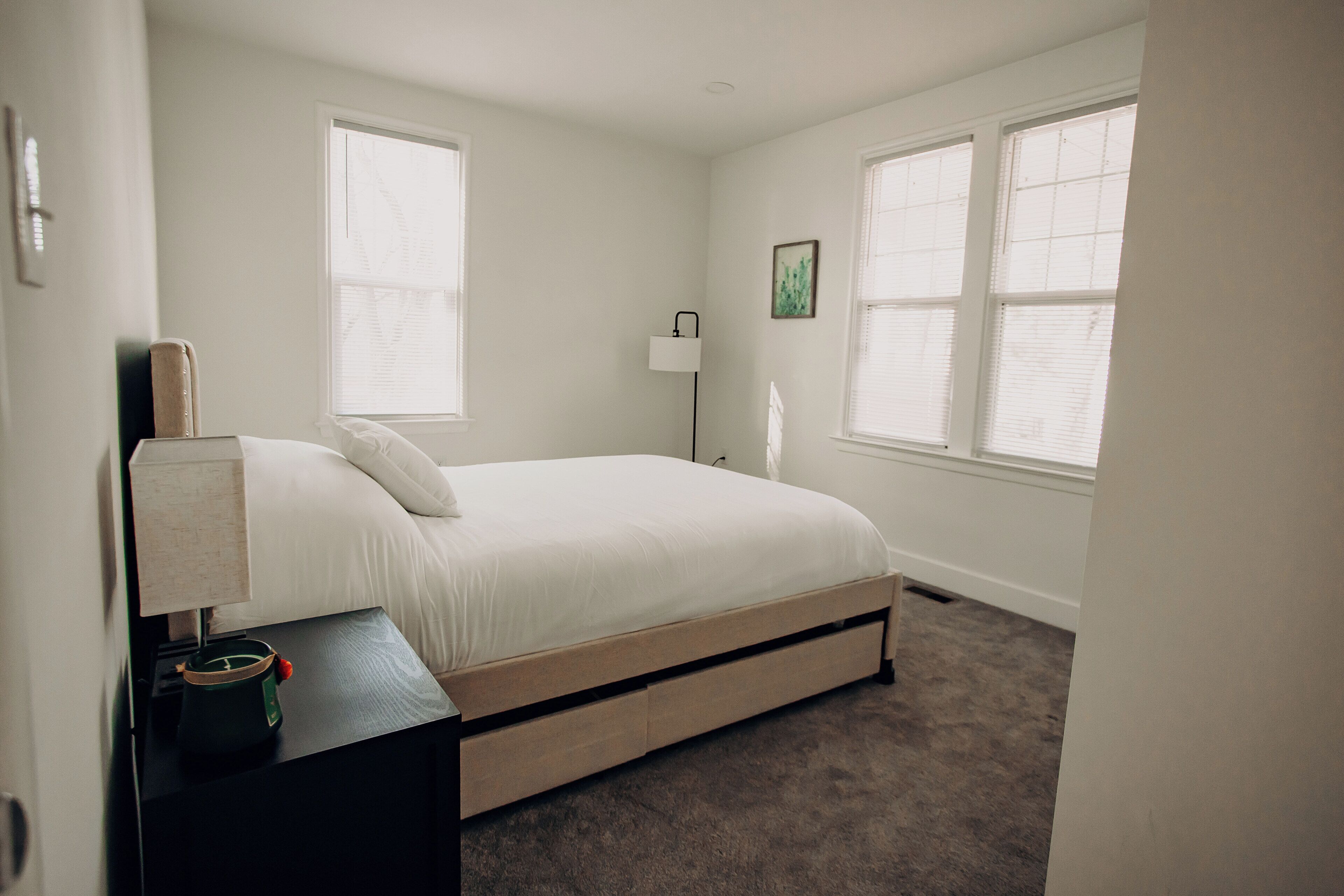 A bedroom with a bed, a nightstand, a lamp, and a window.