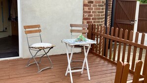Eine Terrasse mit zwei Holzstühlen und einem kleinen Tisch, einem Holzzaun und einer Ziegelwand.