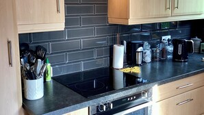 Eine moderne Küche mit hellen Holzschränken, einer schwarzen Arbeitsplatte und Edelstahlgeräten, darunter ein Backofen und ein Geschirrspüler.
