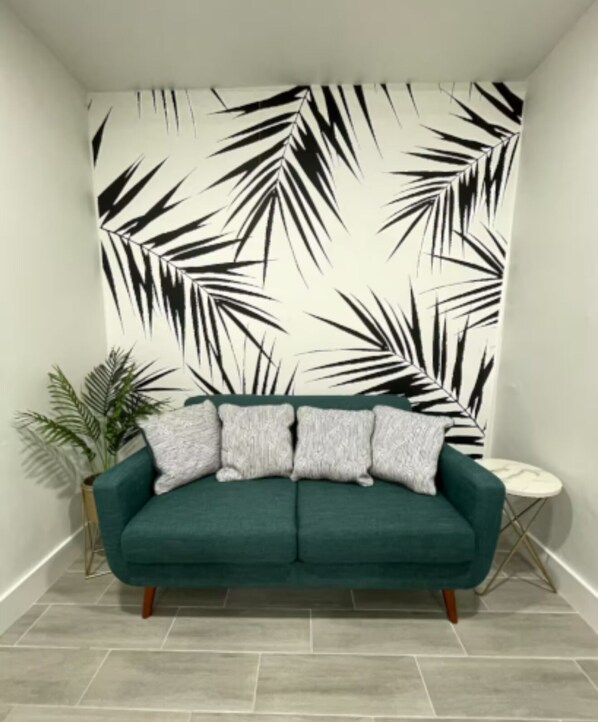 A teal sofa with three pillows against a wall with a black and white leaf pattern.