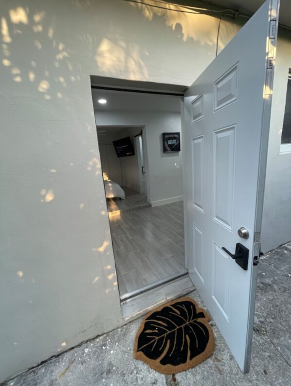 A hallway with a white door, a black doorbell, and a black and brown doormat.