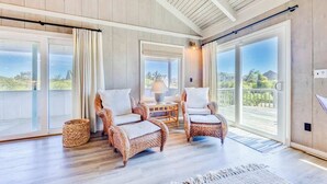 A spacious balcony with wicker chairs and a table, large sliding glass doors, and a view of the outdoors.