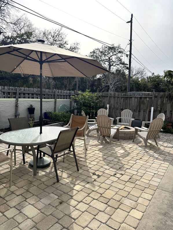 An outdoor patio with a round table, chairs, and a fire pit.