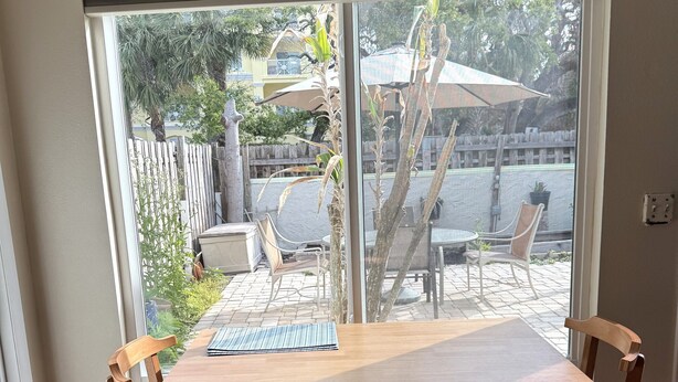 A dining area with a wooden table and chairs, a view through a glass door to an outdoor patio with chairs and a table, and an air conditioning unit above the door.