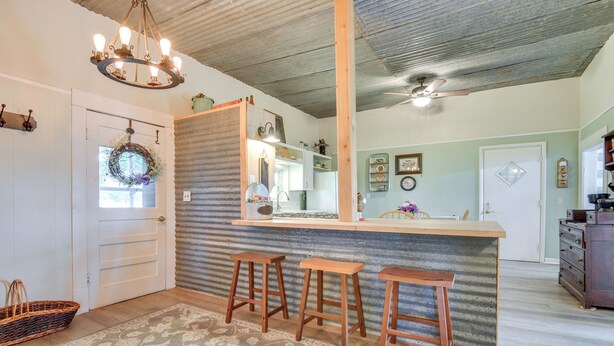 Una cucina con un bancone in legno, tre sgabelli, un lampadario e una ventola a soffitto.