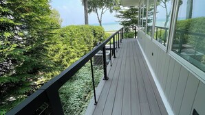 Une terrasse en bois avec une rambarde noire, offrant une vue sur un paysage verdoyant et luxuriant ainsi que sur une étendue d’eau.