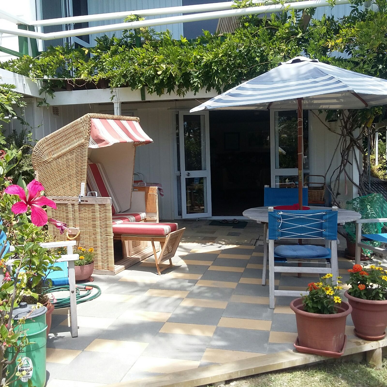 An outdoor patio with a table, chairs, a wicker chair with a striped canopy, and potted plants.