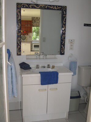 A bathroom with a white sink, a mirror with a floral frame, and a blue towel hanging on the wall. - Peaceful 1-bedroom apartment in charming Russell perfect fora relaxing stay (Russell)