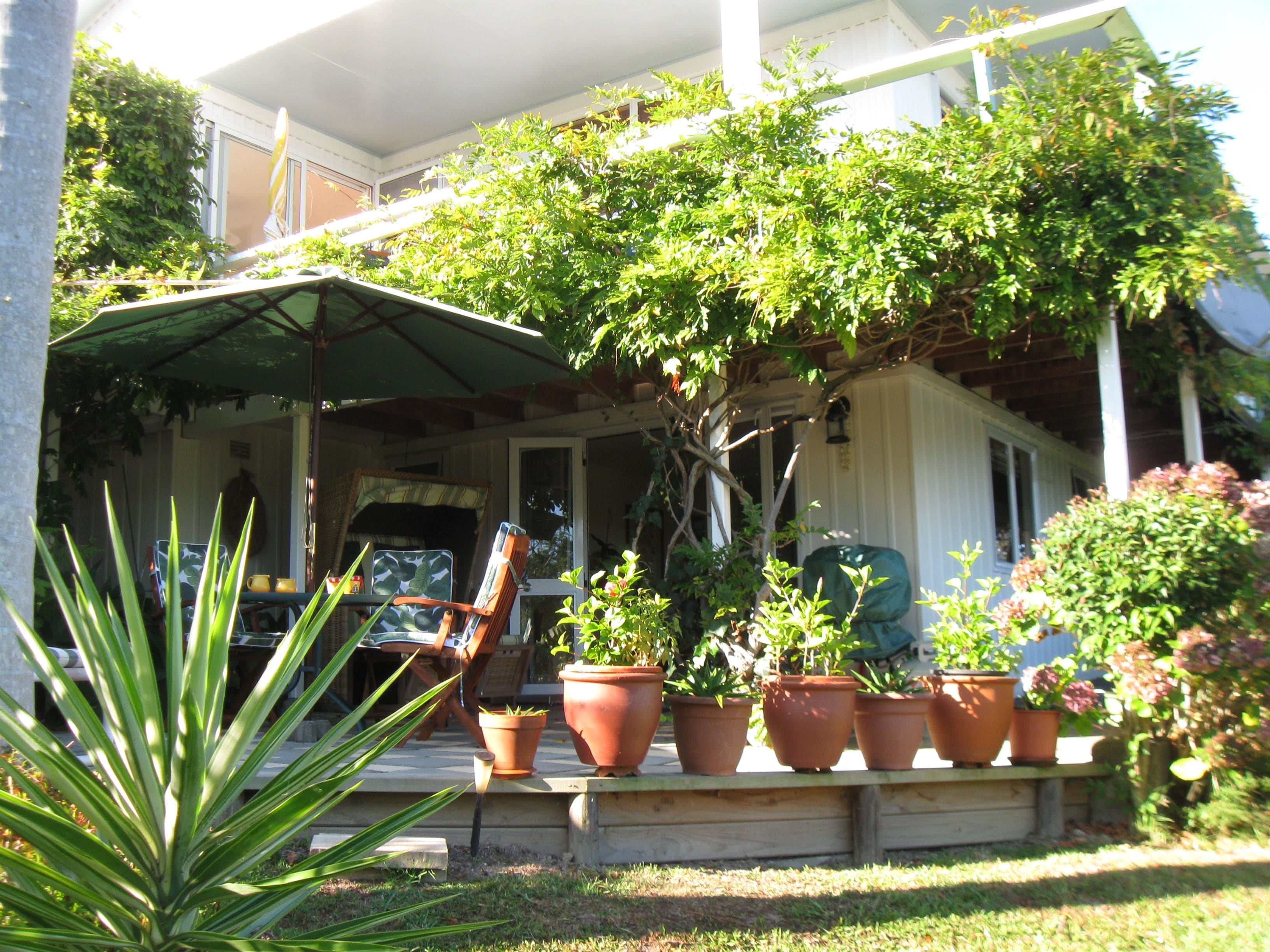 A covered porch with outdoor furniture, potted plants, and a lawn.