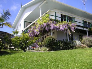 A white building with green trim and a large tree with purple flowers in front. - Peaceful 1-bedroom apartment in charming Russell perfect fora relaxing stay (Russell)