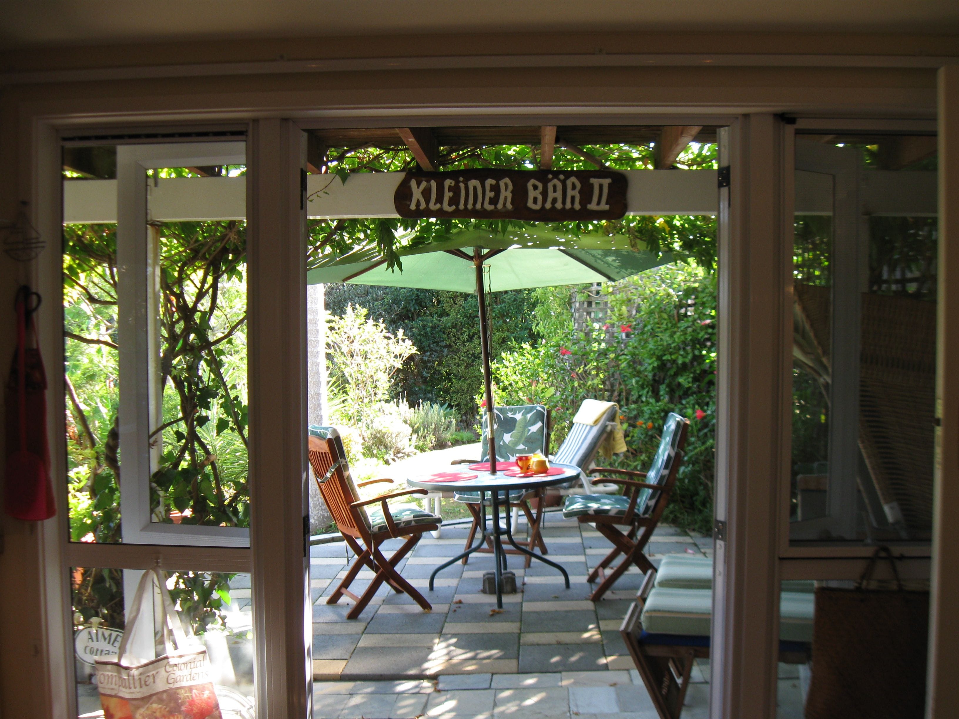 An outdoor seating area with a table and chairs under a green umbrella, labeled 'KLEINER BAR II'.