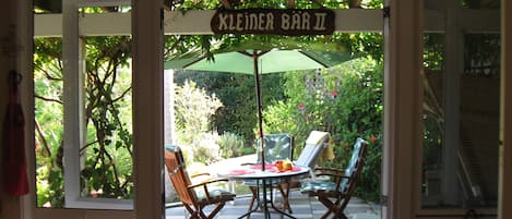 An outdoor seating area with a table and chairs under a green umbrella, labeled 'KLEINER BAR II'.