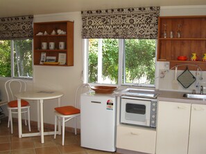 Een compacte keuken met een koelkast, magnetron en een klein eethoekje met twee stoelen.
