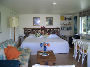 A bedroom with a bed, a bedside table, a chair, a small table with a vase of flowers, and a bookshelf. - Peaceful 1-bedroom apartment in charming Russell perfect fora relaxing stay (Russell)