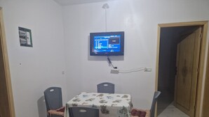 A dining area with a table and four chairs, a wall-mounted television, and a power outlet. - Air-conditioned apartment for rent in SAÏDIA (Saïdia)