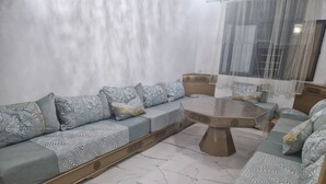 A modern living room with a sofa set, a round coffee table, and a patterned floor. - Air-conditioned apartment for rent in SAÏDIA (Saïdia)