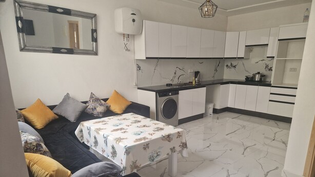 A compact living space with a sofa, a small table, a washing machine, and a kitchen area. - Air-conditioned apartment for rent in SAÏDIA (Saïdia)