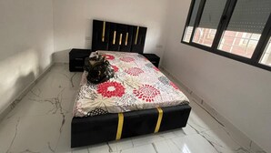 A bedroom with a bed, a nightstand, a decorative vase, and a window with blinds. - Air-conditioned apartment for rent in SAÏDIA (Saïdia)