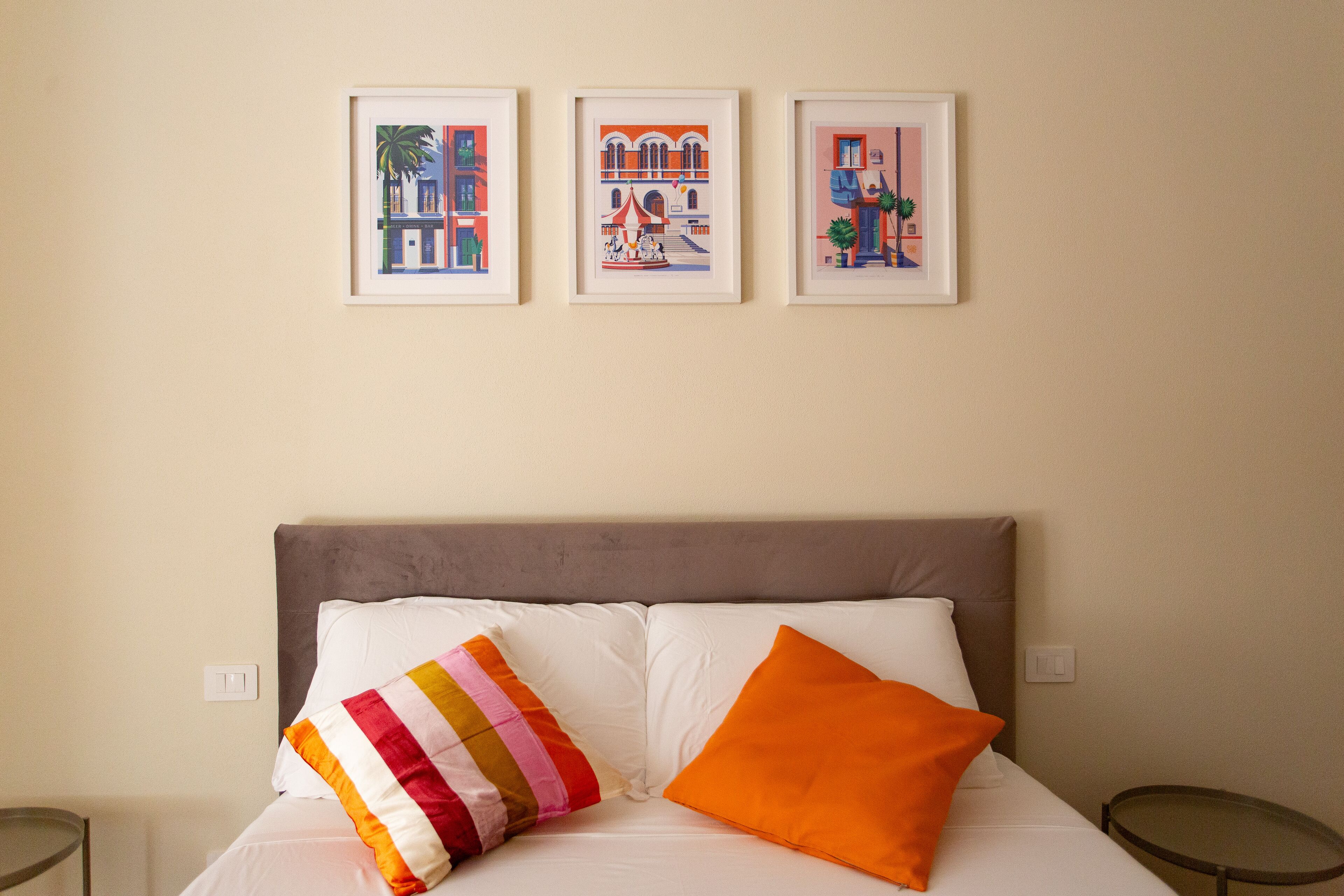 Una cama con ropa de cama blanca y dos almohadas, un cabecero gris y tres cuadros enmarcados en la pared de arriba.