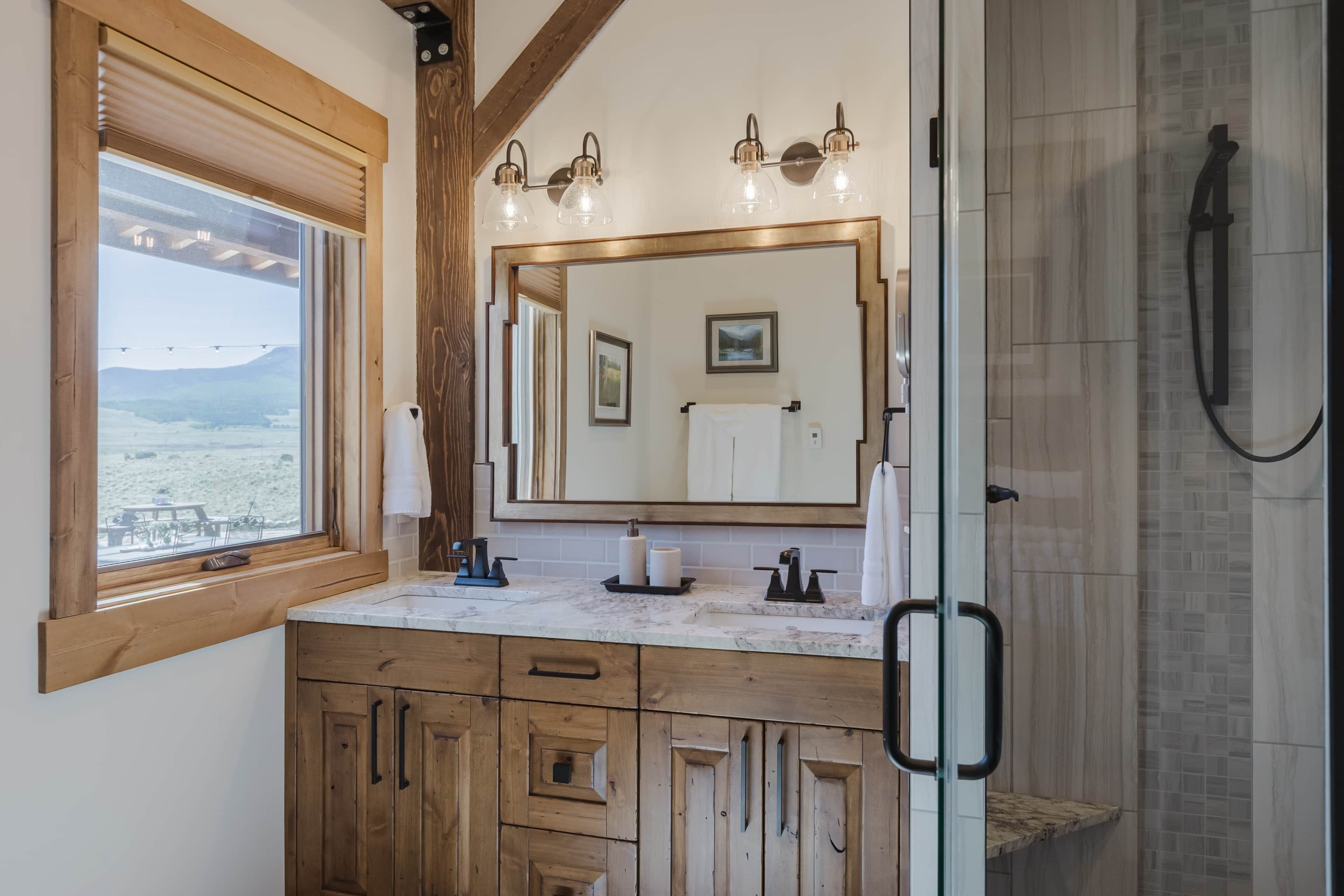 A bathroom with a large mirror, wooden cabinets, a sink, and a shower.