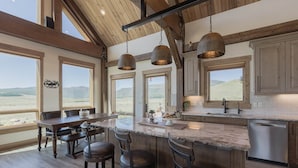 Una cocina amplia con una isla grande, armarios de madera y ventanas panorámicas que ofrecen vistas del paisaje.