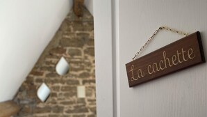 Un dormitorio con una puerta blanca, un letrero de madera que dice 'la cachette' y una pared de piedra al fondo.