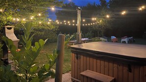 Un jacuzzi con plataforma de madera, rodeado de luces cálidas y follaje.