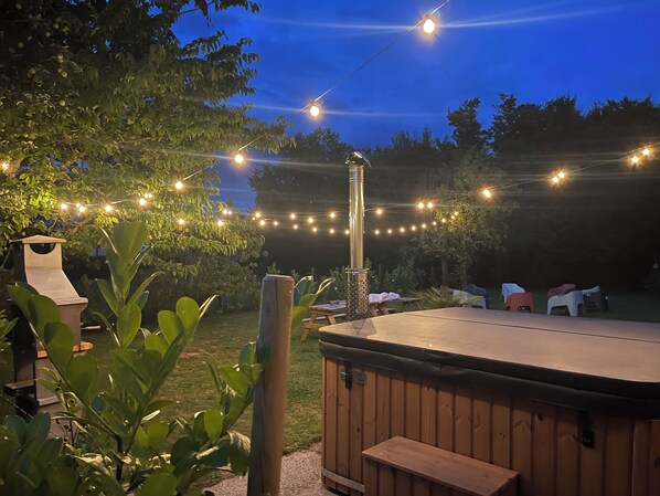 A hot tub with a wooden deck, surrounded by string lights and greenery.