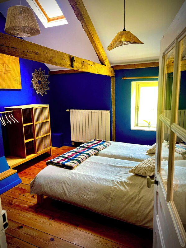 A bedroom with two beds, wooden beams, a radiator, a wardrobe, and a window with natural light.