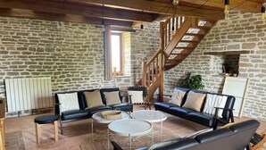 Una sala de estar acogedora con una pared de piedra, una escalera de madera y un sofá de cuero negro.