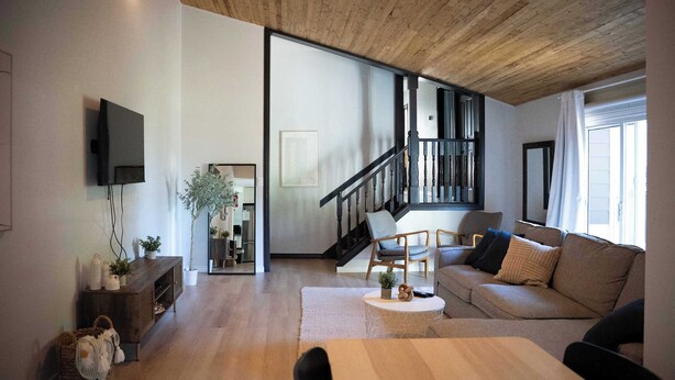 Ein modernes Wohnzimmer mit Holzboden, einer Treppe, einem Sofa, einem Couchtisch und einem an der Wand befestigten Fernseher.