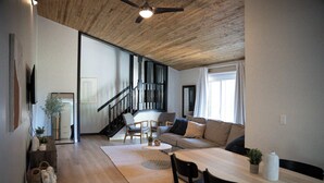 Ein geräumiger Wohnbereich mit Holzboden, einer Treppe, einer Couch, einem Esstisch und einem an der Wand befestigten Fernseher.