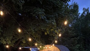 Eine Holzhütte mit gewölbtem Dach, umgeben von viel Grün und Lichterketten.