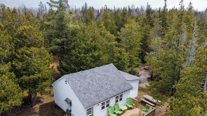 A white cabin with a deck, surrounded by dense forest.