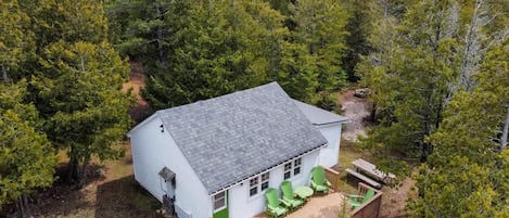 Una cabaña blanca con terraza, rodeada de un bosque denso.
