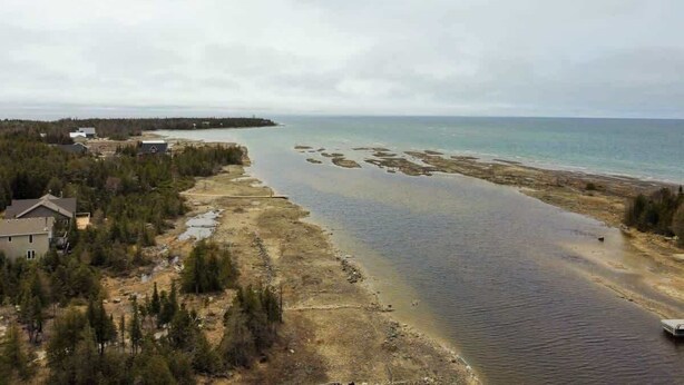 A coastal area with a river leading to the sea, surrounded by trees and a few buildings.