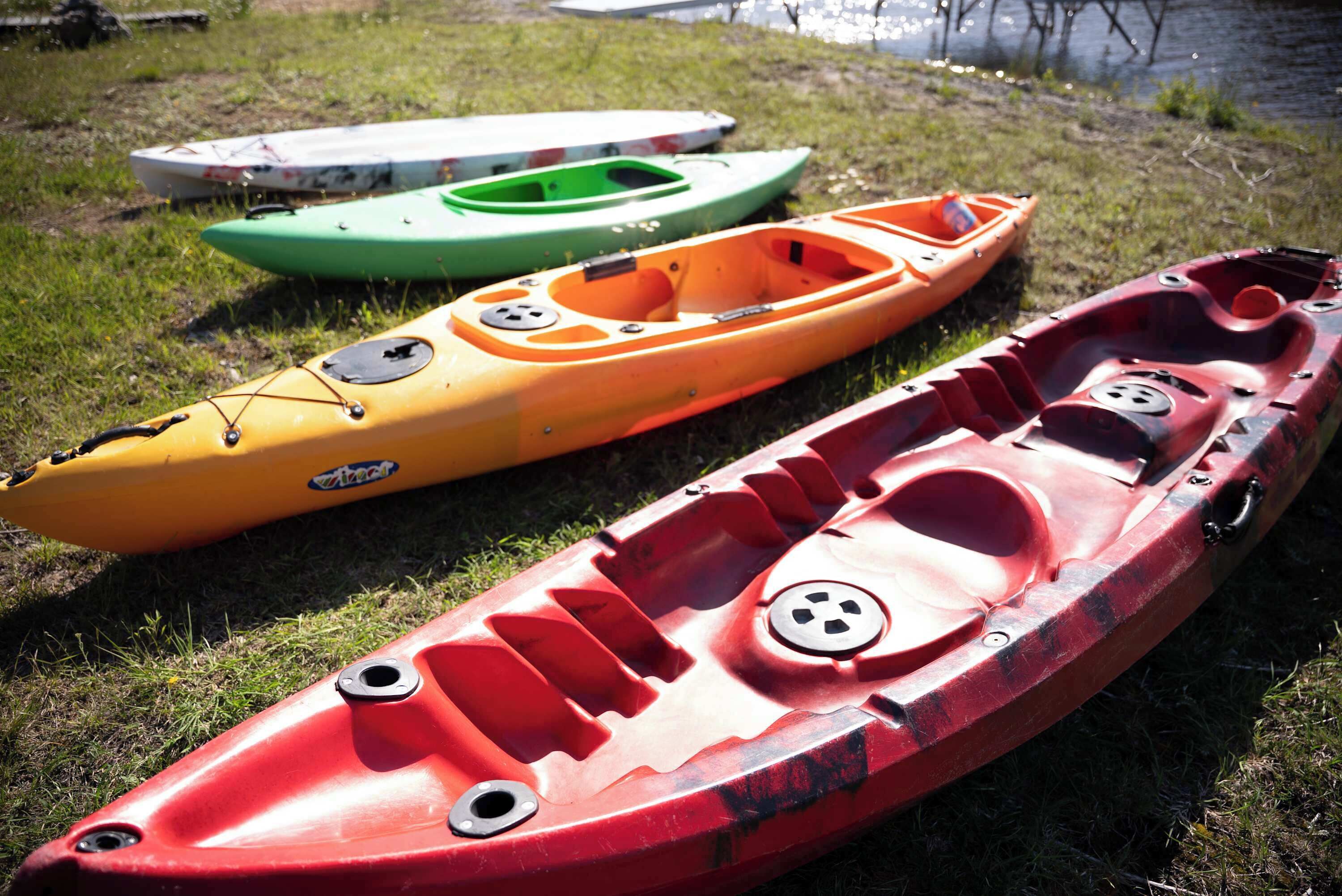 Three kayaks on grass near a body of water.