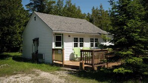 A small, single-story cabin with a porch and two green Adirondack chairs.