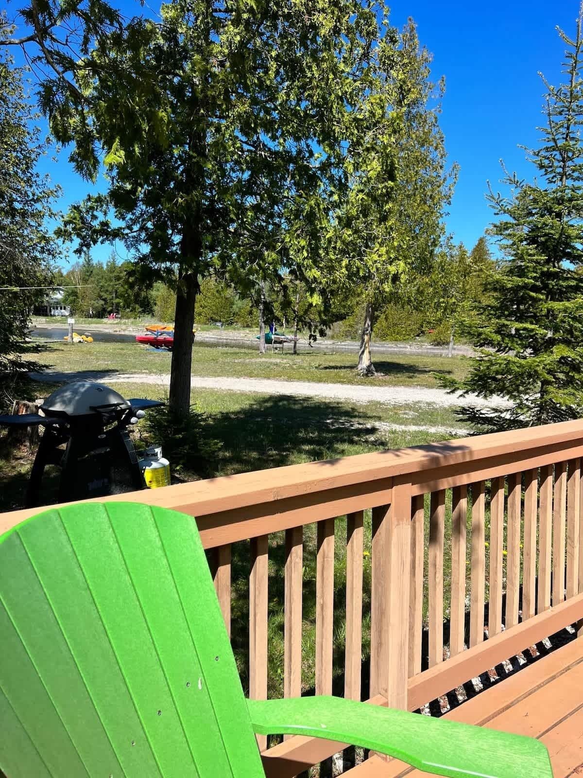 Eine Holzterrasse mit einem grünen Stuhl, einem Grill und Bäumen im Hintergrund.