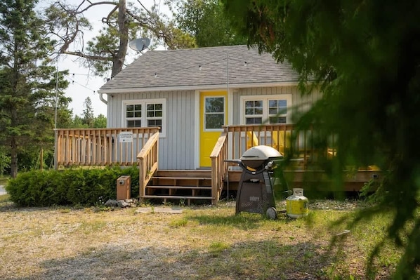 A small cabin with a yellow door, wooden deck, and a grill.