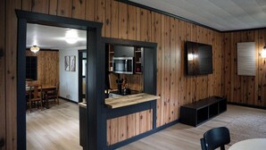 A modern kitchen with wooden paneling, a built-in microwave, and a dining area with a wooden table and chairs.