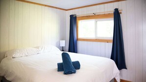 Una cama bien hecha con sábanas blancas y dos toallas azules enrolladas encima.