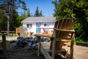 A wooden Adirondack chair in a garden area with a house in the background. - Cozy 2‑Bed Waterfront Cabin | Near Bruce Peninsula (Tobermory)